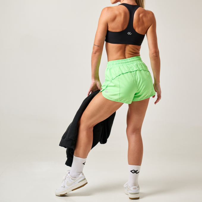Woman wearing a black sports bra and green shorts with a white background