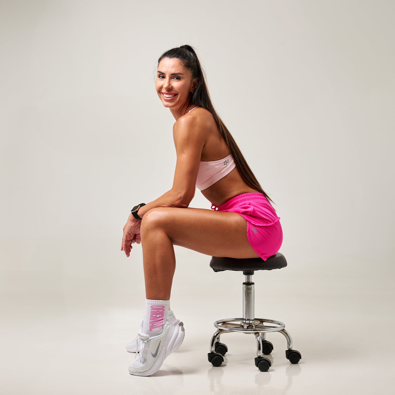 Woman in pink athletic wear sitting on a black office chair against a white background