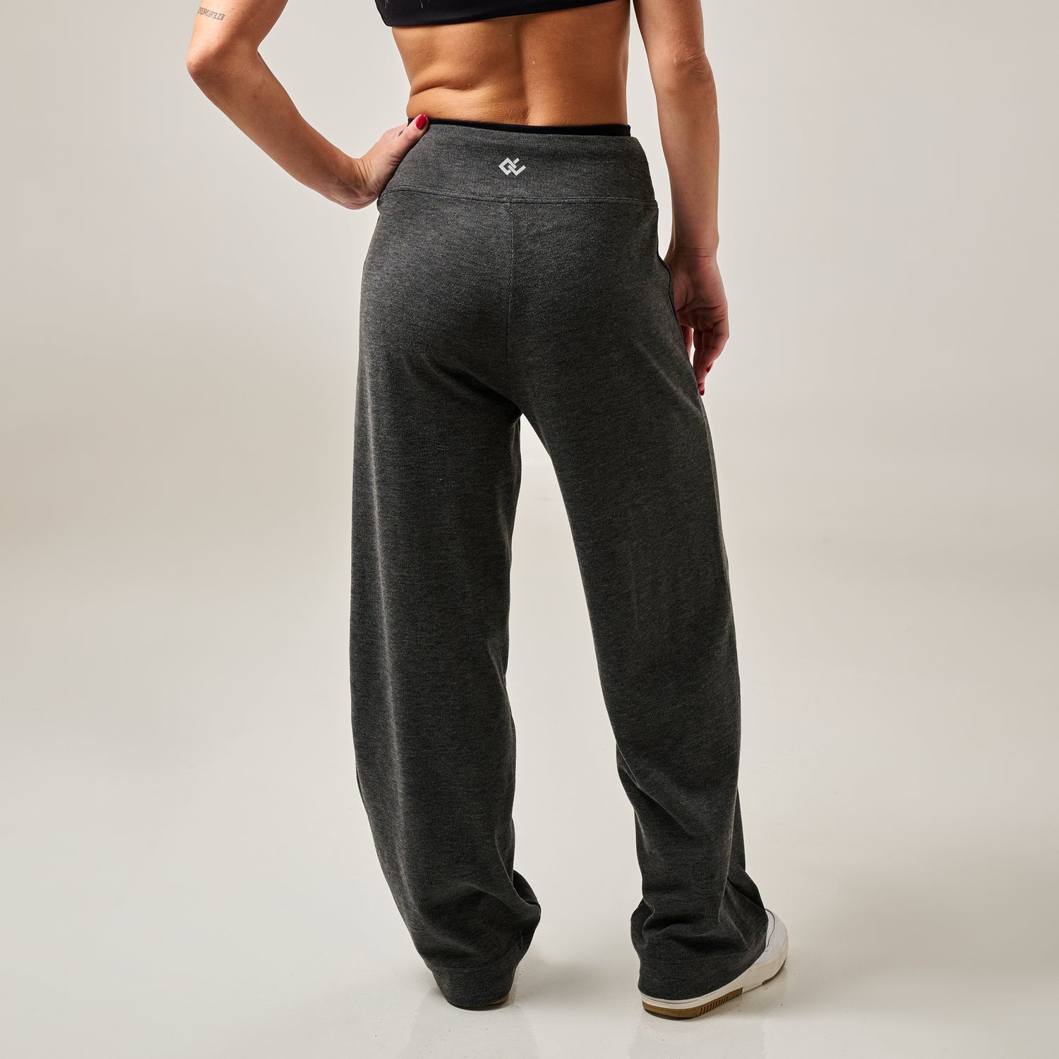 Woman wearing dark grey sweatpants on a plain background