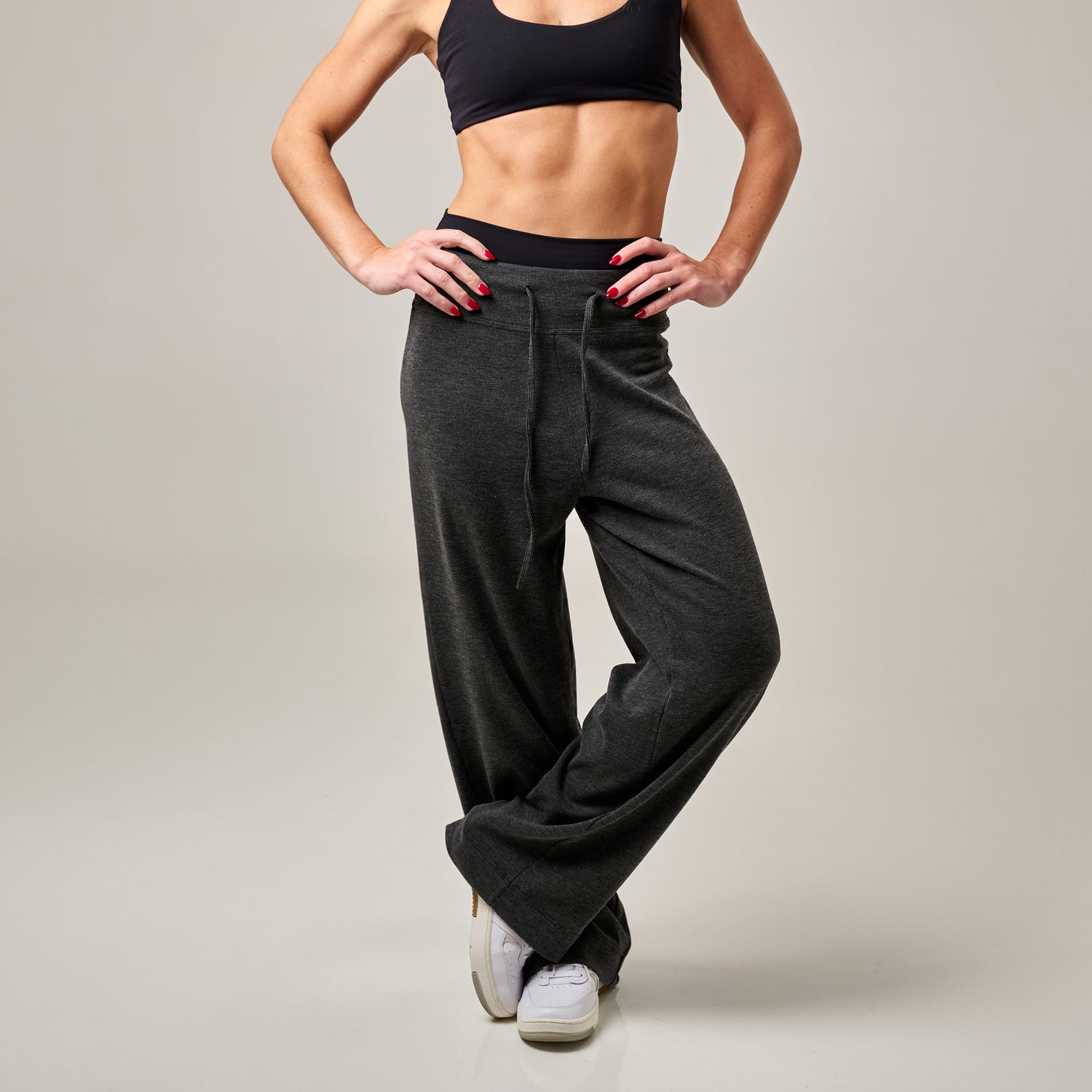 Woman wearing a black sports bra and wide-leg gray pants on a plain background